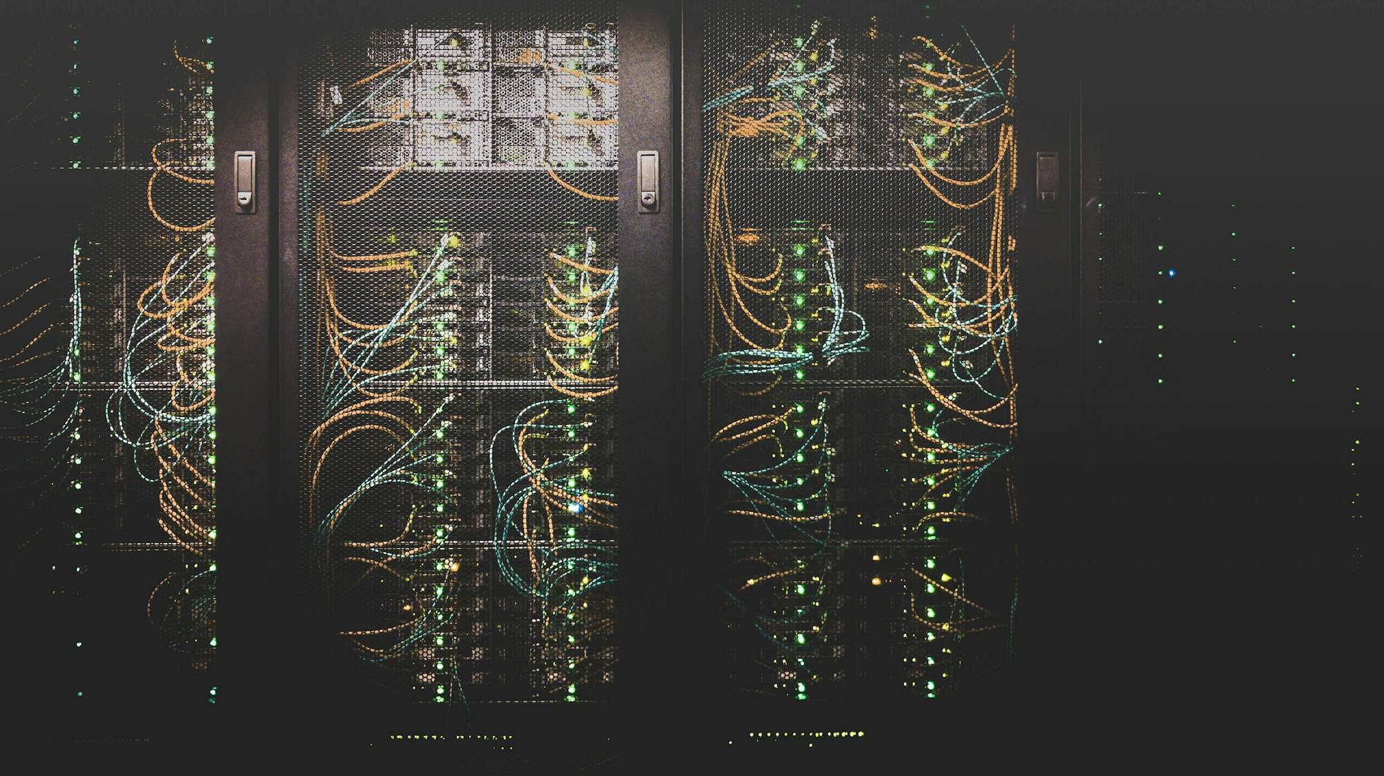 Server-Racks mit farbigen Netzwerkkabeln in einem abgedunkelten Rechenzentrum