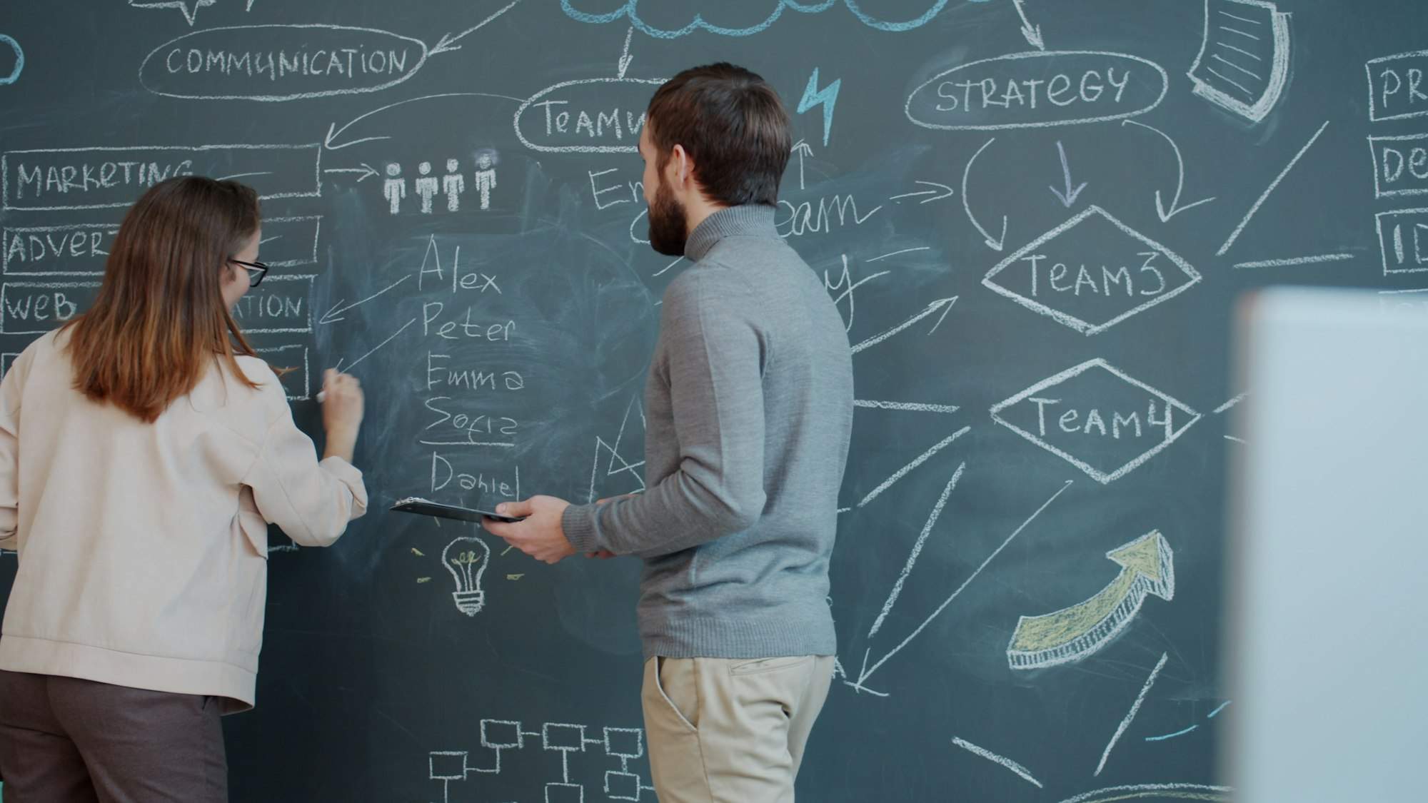 Zwei Personen planen an einer Tafel voller Diagramme